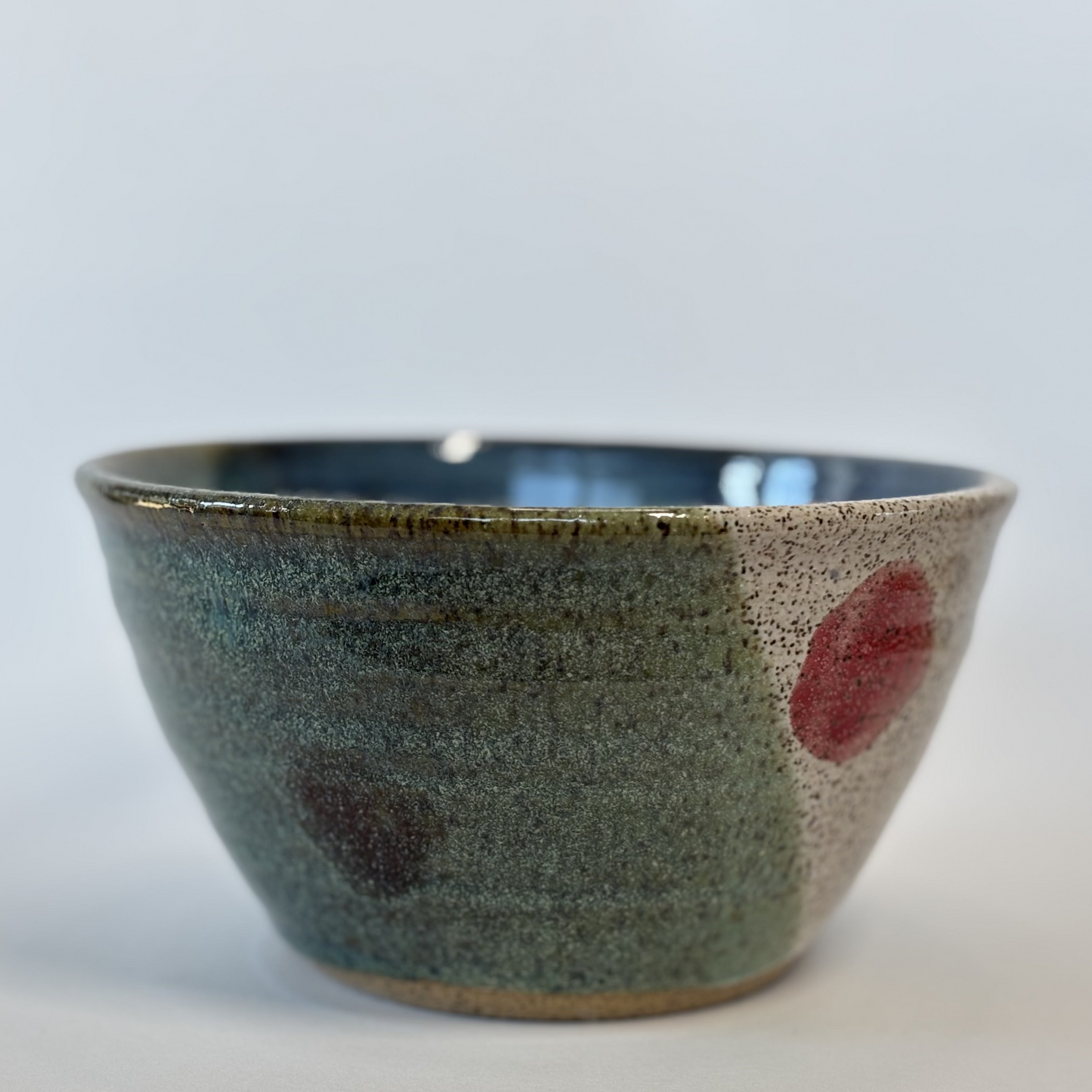 Ceramic bowl with speckled glaze and red spots on a white background