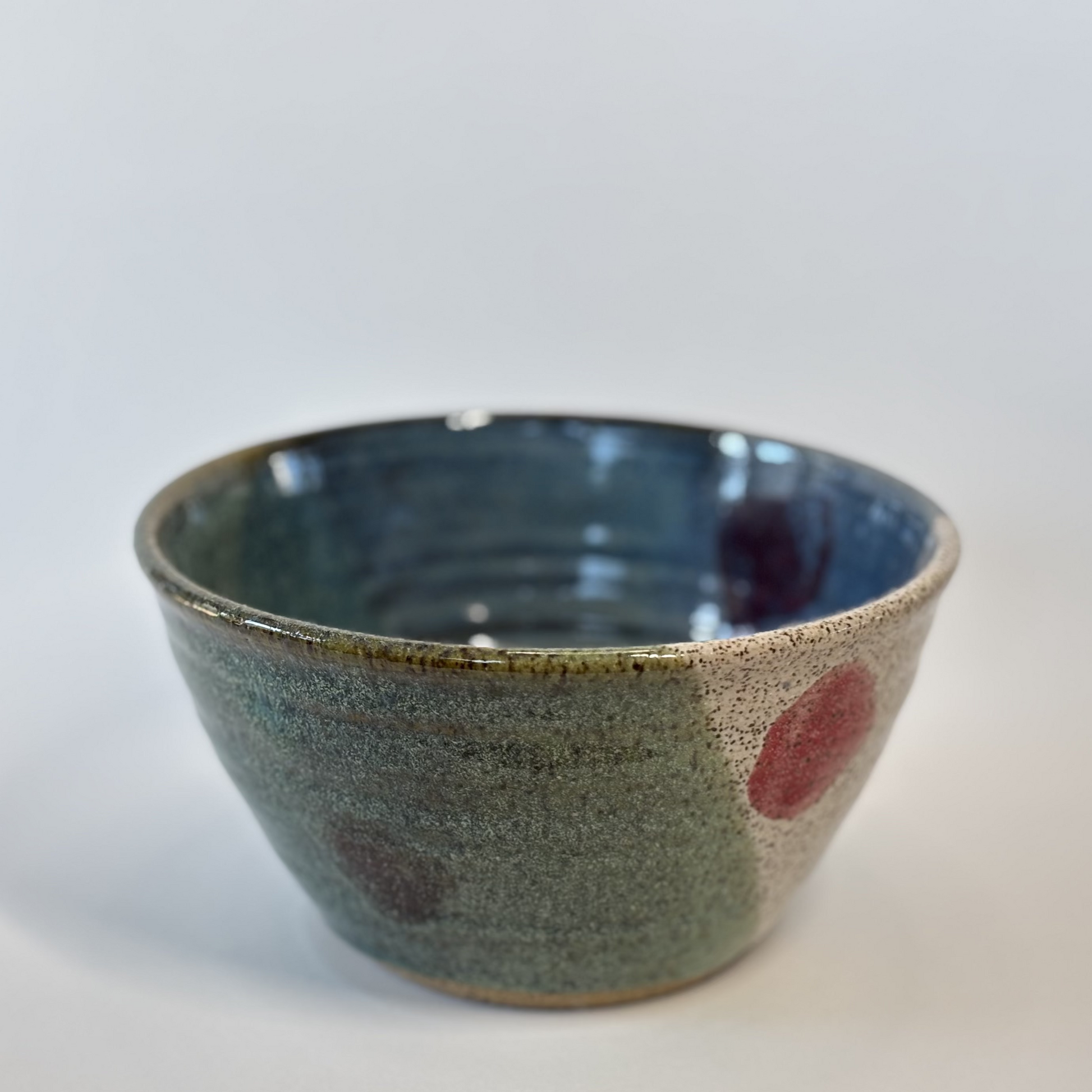 Ceramic bowl with speckled glaze and red accents on a white background